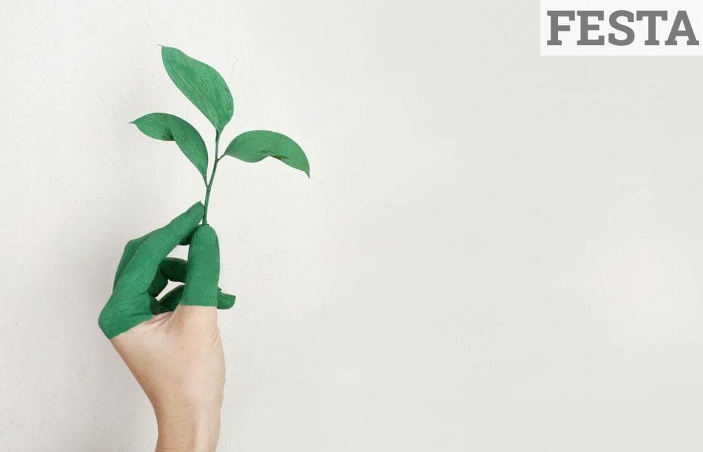A hand painted green holds a fresh plant sprout against a light background, symbolizing growth and sustainability.